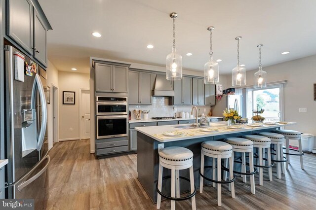 11726 Robin Woods Cir, Spotsylvania, VA 22551 - kitchen featuring appliances with stainless steel finishes, gray cabinetry, wall chimney exhaust hood, a sink, and light wood-style floors