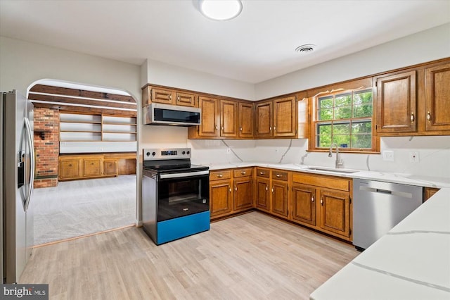 kitchen with stainless steel appliances, light wood-style flooring, brown cabinets, a sink, and light stone countertops