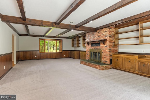 unfurnished living room featuring light carpet, wood walls, wainscoting, and beamed ceiling
