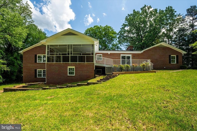 rear view of house featuring a sunroom, brick siding, a wooden deck, and a yard