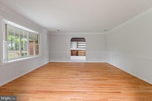 unfurnished room with ornamental molding, light wood-style flooring, baseboards, and arched walkways