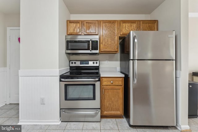 10108 Chesney Dr, Spotsylvania, VA 22553 - kitchen featuring appliances with stainless steel finishes, wainscoting, brown cabinetry, light countertops, and light tile patterned flooring