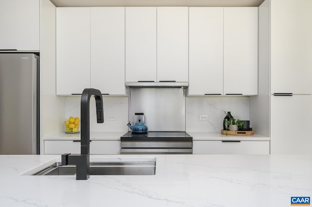 kitchen with freestanding refrigerator, a sink, white cabinetry, and backsplash