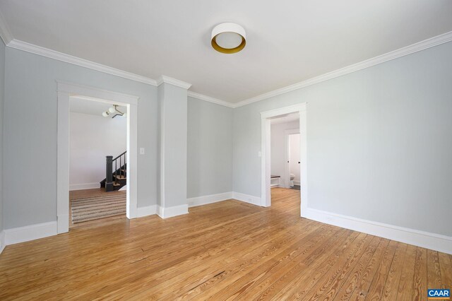 spare room with crown molding, light wood-style floors, baseboards, and stairway