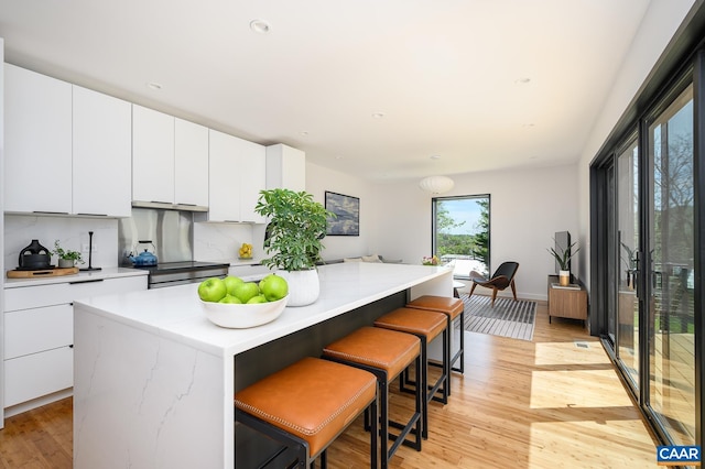 kitchen featuring light wood-style floors, a center island, a kitchen breakfast bar, light countertops, and white cabinets