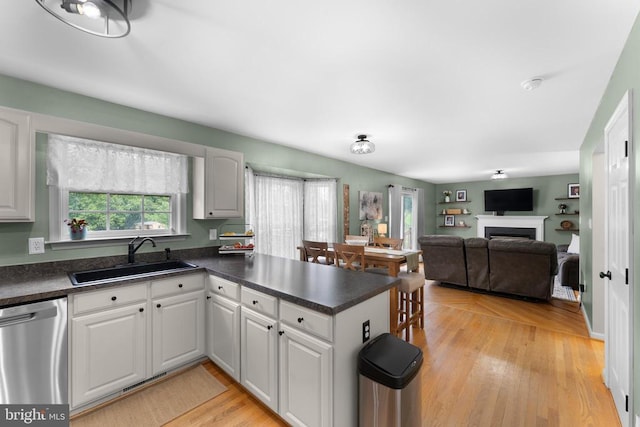  - kitchen featuring stainless steel dishwasher, dark countertops, a peninsula, light wood finished floors, and white cabinets