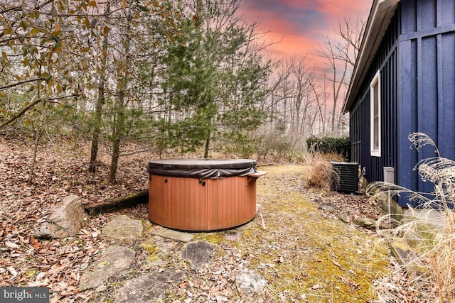 yard at dusk with a hot tub and central AC