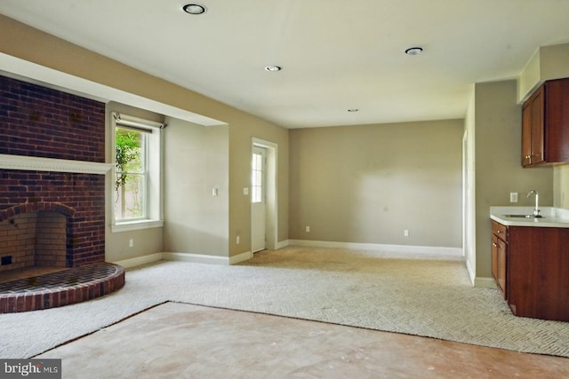 unfurnished living room with a sink, light carpet, a fireplace, and baseboards