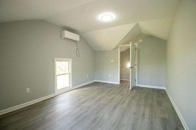 additional living space featuring an AC wall unit, lofted ceiling, wood finished floors, and baseboards
