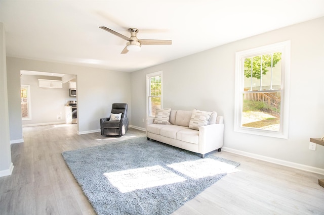 living area featuring light wood-style floors, ceiling fan, plenty of natural light, and baseboards