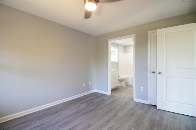 unfurnished bedroom featuring wood finished floors, baseboards, ensuite bathroom, and ceiling fan
