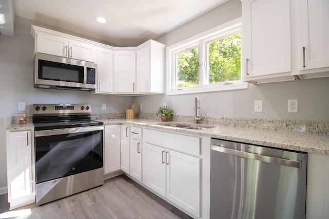 kitchen featuring stainless steel appliances, a sink, white cabinets, light wood-type flooring, and light stone countertops