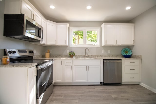 kitchen with appliances with stainless steel finishes, a sink, white cabinetry, recessed lighting, and light wood-type flooring