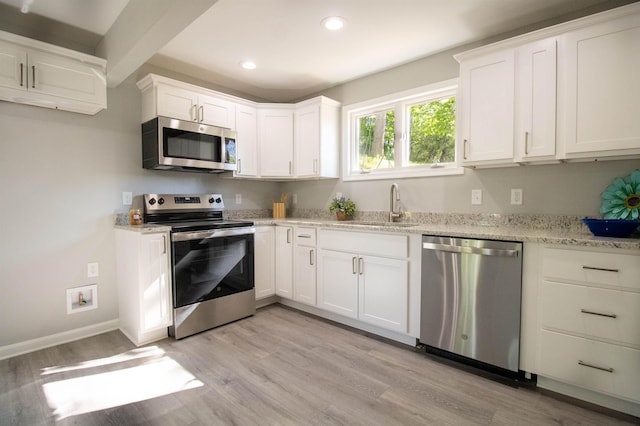 kitchen with appliances with stainless steel finishes, a sink, recessed lighting, light wood-style flooring, and light stone counters