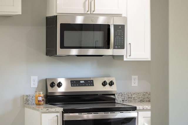 kitchen view of appliances with stainless steel finishes, white cabinets, and light stone countertops