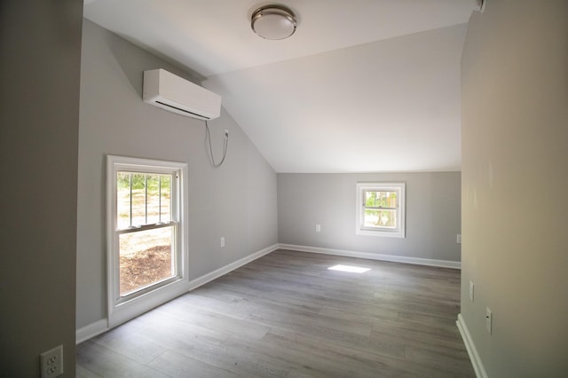 bonus room featuring an AC wall unit, plenty of natural light, lofted ceiling, wood finished floors, and baseboards