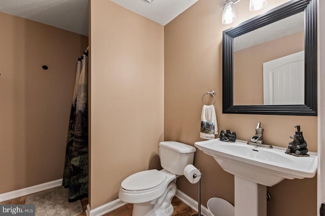 bathroom featuring a shower with shower curtain, toilet, and baseboards