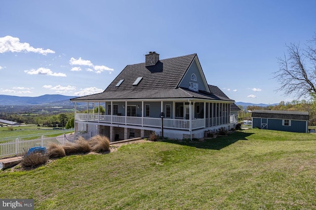 rear view of property with an outbuilding, a mountain view, a chimney, fence, and a yard