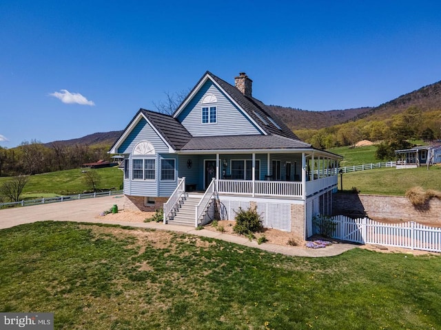 farmhouse inspired home featuring a chimney, a porch, a front lawn, and a mountain view
