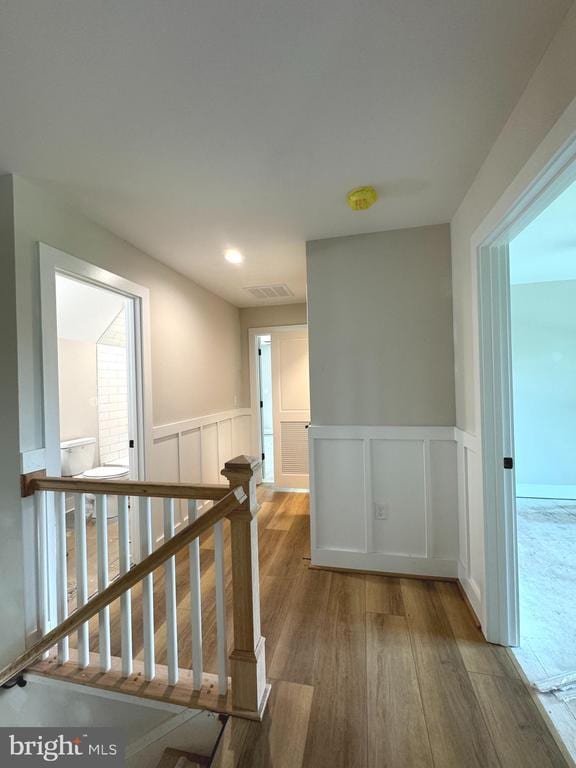  - hallway featuring wood finished floors, wainscoting, an upstairs landing, and a decorative wall