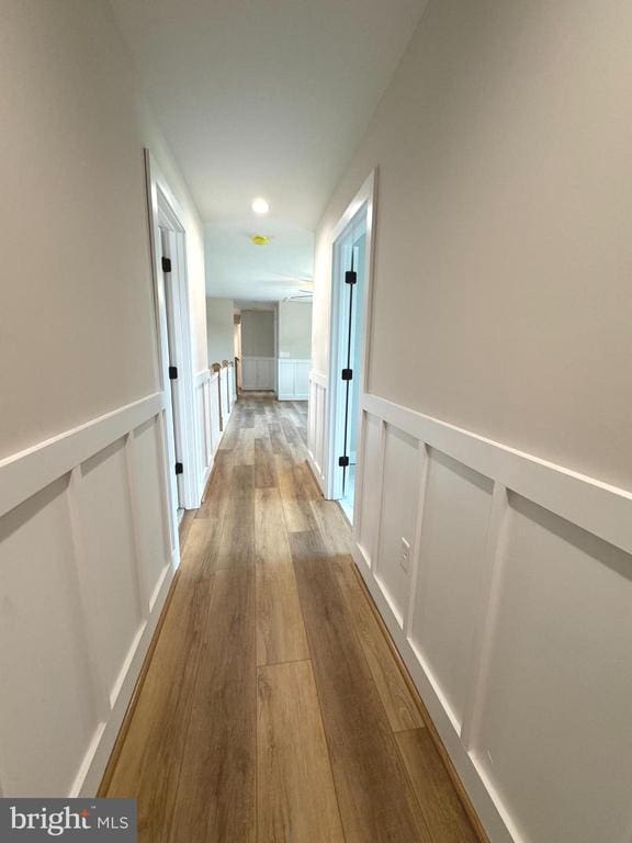  - hall with wood finished floors, wainscoting, a decorative wall, and recessed lighting