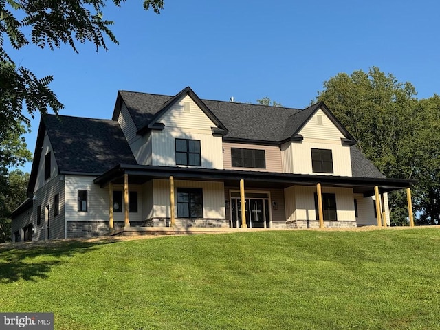  - rear view of property featuring covered porch, a lawn, stone siding, and roof with shingles