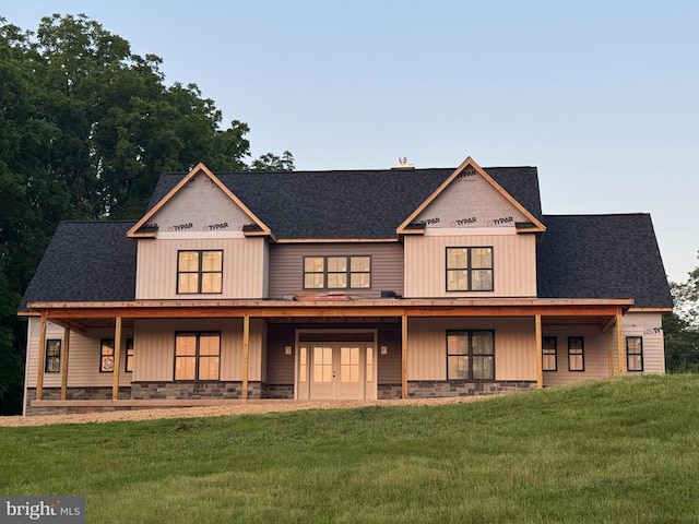  - view of front of house with a front lawn, stone siding, covered porch, and roof with shingles