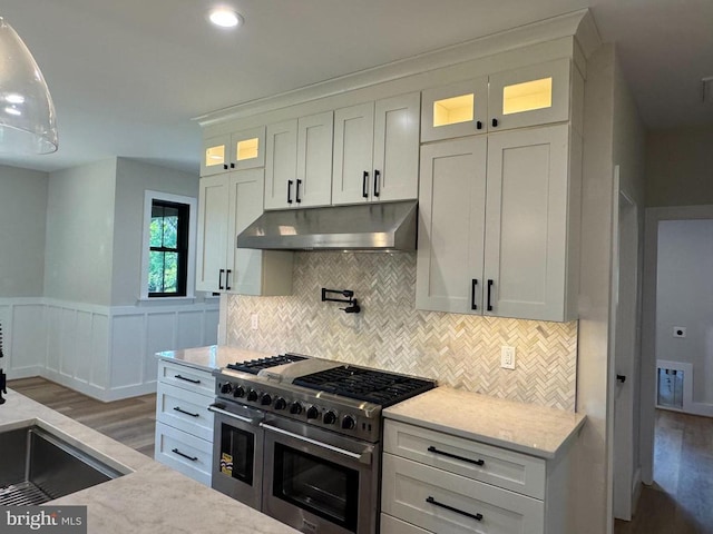  - kitchen featuring range with two ovens, under cabinet range hood, wood finished floors, backsplash, and white cabinetry