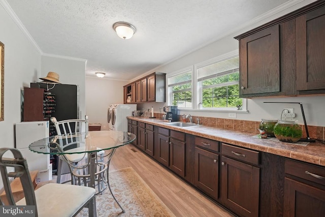  - kitchen featuring washer and clothes dryer, ornamental molding, light wood-style flooring, dark brown cabinets, and a textured ceiling