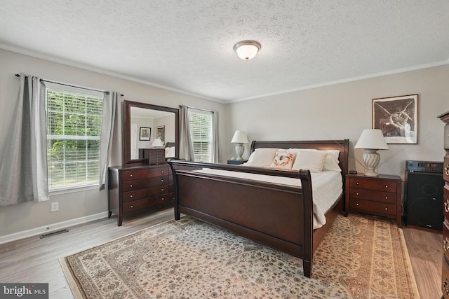  - bedroom featuring multiple windows, light wood-style flooring, a textured ceiling, and ornamental molding