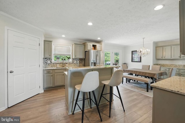  - kitchen featuring stainless steel fridge with ice dispenser, ornamental molding, a center island, a kitchen bar, and a chandelier