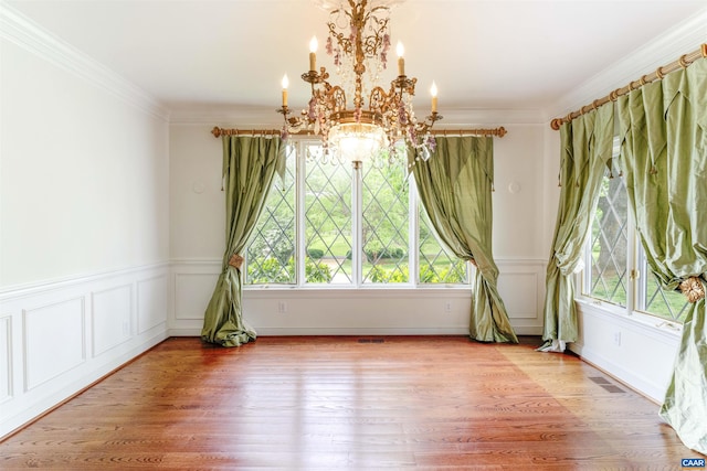 unfurnished dining area with a chandelier, wood finished floors, crown molding, and wainscoting