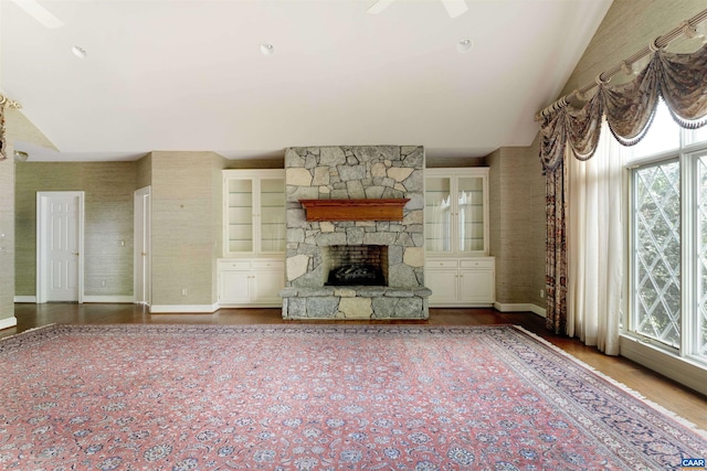 unfurnished living room with healthy amount of natural light, baseboards, lofted ceiling, a stone fireplace, and wood finished floors