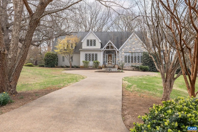 new england style home with stone siding, a front lawn, and stucco siding