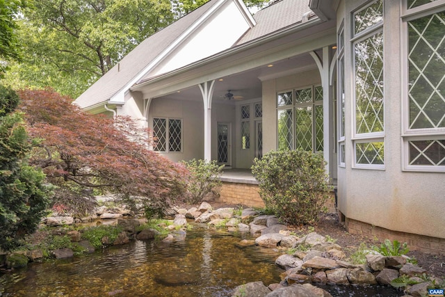 view of exterior entry featuring a ceiling fan, stucco siding, and a shingled roof