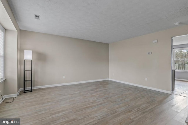 spare room with light wood-style floors, a textured ceiling, and baseboards