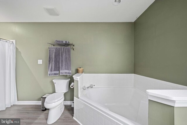 full bathroom featuring toilet, a bath, wood finished floors, and baseboards