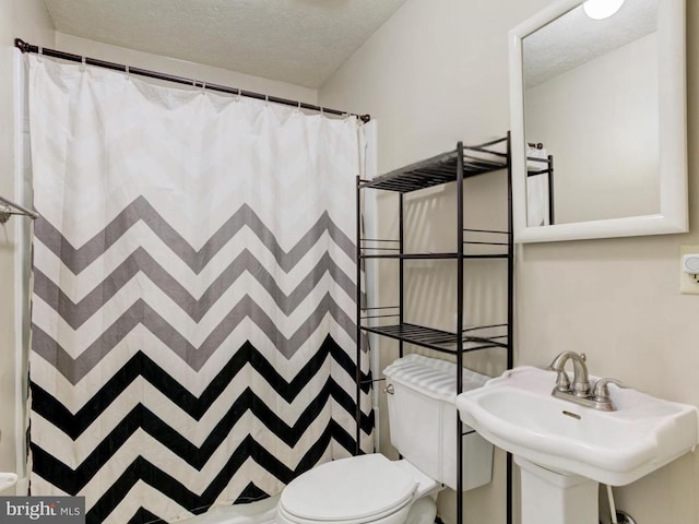 full bath with a textured ceiling, a shower with shower curtain, toilet, and a sink