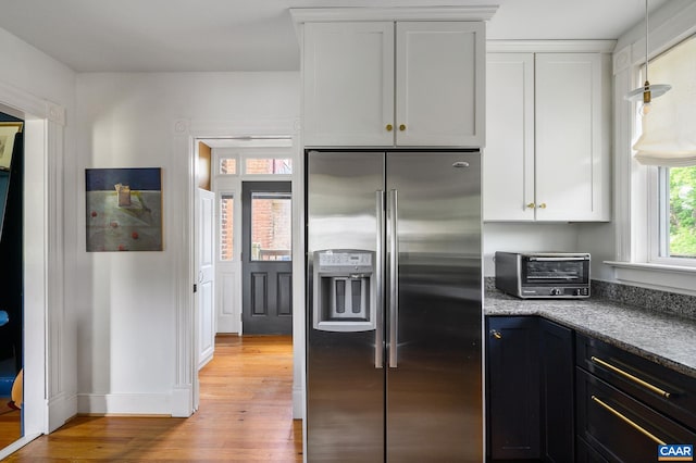 kitchen featuring stainless steel fridge with ice dispenser, light wood finished floors, white cabinetry, and pendant lighting