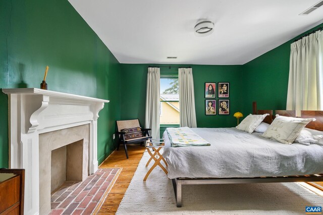 bedroom featuring a fireplace with flush hearth, wood finished floors, and baseboards