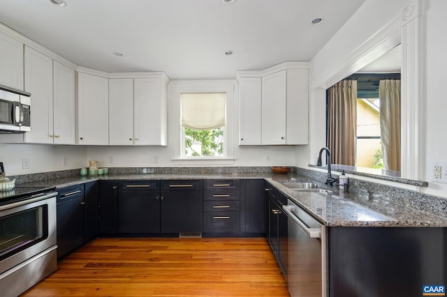 kitchen featuring appliances with stainless steel finishes, a sink, white cabinetry, dark stone counters, and recessed lighting
