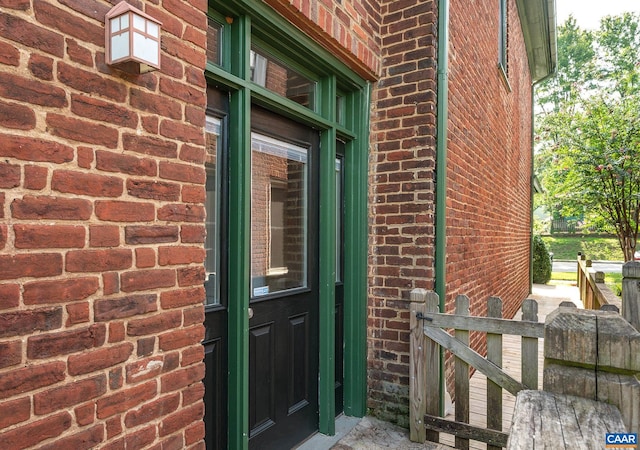 view of exterior entry featuring brick siding and fence