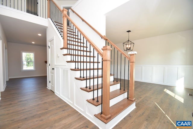 staircase with a decorative wall, visible vents, wood finished floors, and a notable chandelier