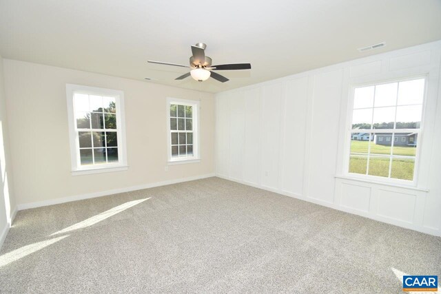 empty room featuring carpet flooring, a decorative wall, a ceiling fan, and visible vents