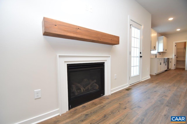 unfurnished living room with wood finished floors, visible vents, recessed lighting, baseboards, and a glass covered fireplace