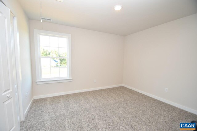 carpeted spare room featuring baseboards, visible vents, and attic access