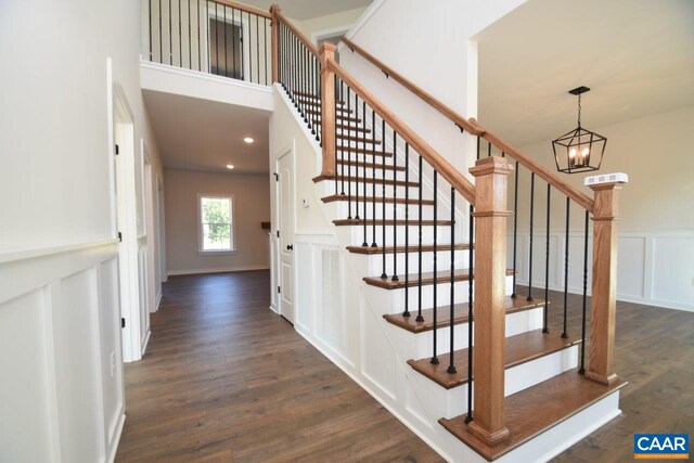 staircase with a chandelier, a decorative wall, a wainscoted wall, and wood finished floors
