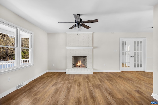 unfurnished living room featuring hardwood / wood-style flooring, ceiling fan, a fireplace, and french doors