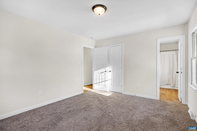 unfurnished bedroom featuring ensuite bathroom, light colored carpet, and a closet