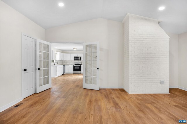 interior space with french doors, sink, vaulted ceiling, and light wood-type flooring